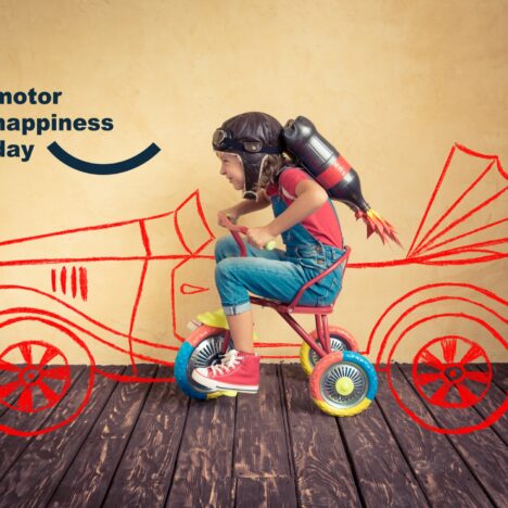 Motor Happiness Day: bambina con casco e razzo su un triciclo davanti a un’auto disegnata